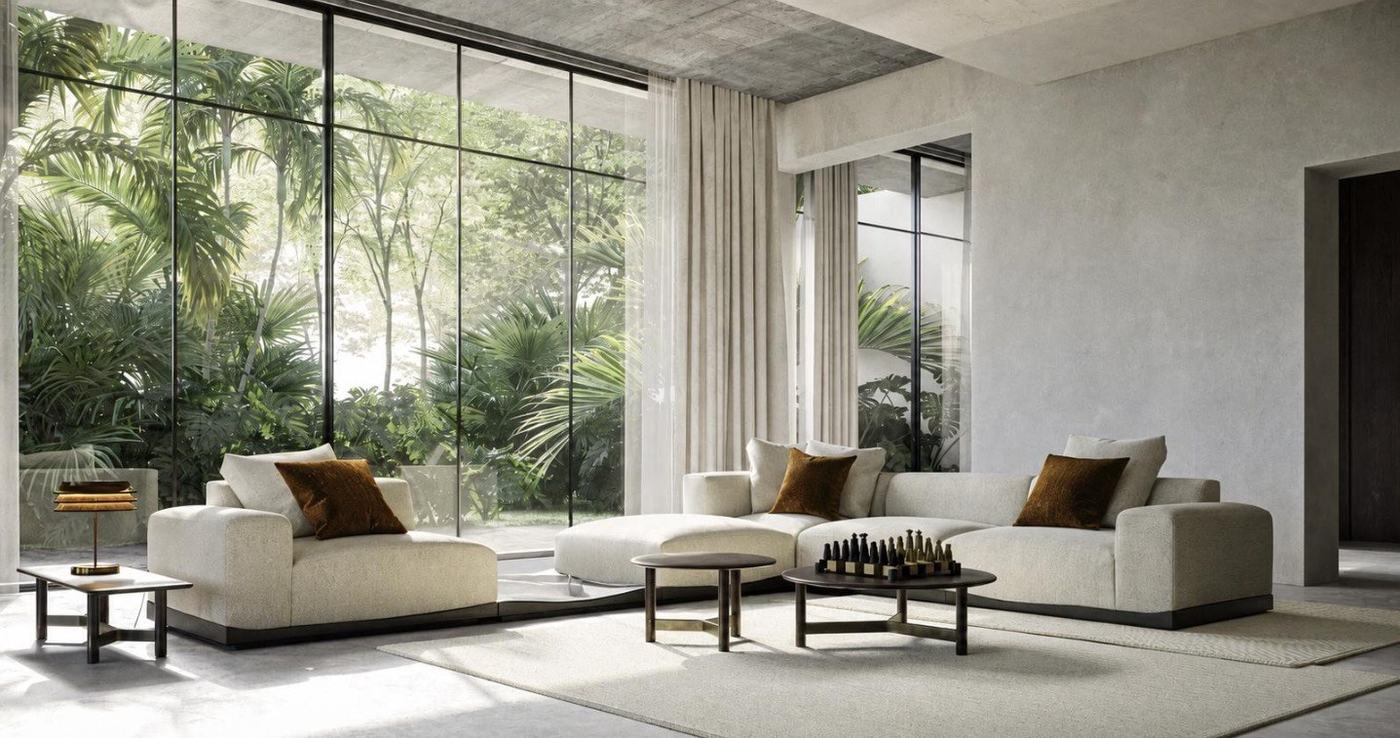A sunlit living room with a low ivory modular sectional, a matching lounge chair, dark round coffee tables on bronze bases and a wall of glass onto a garden