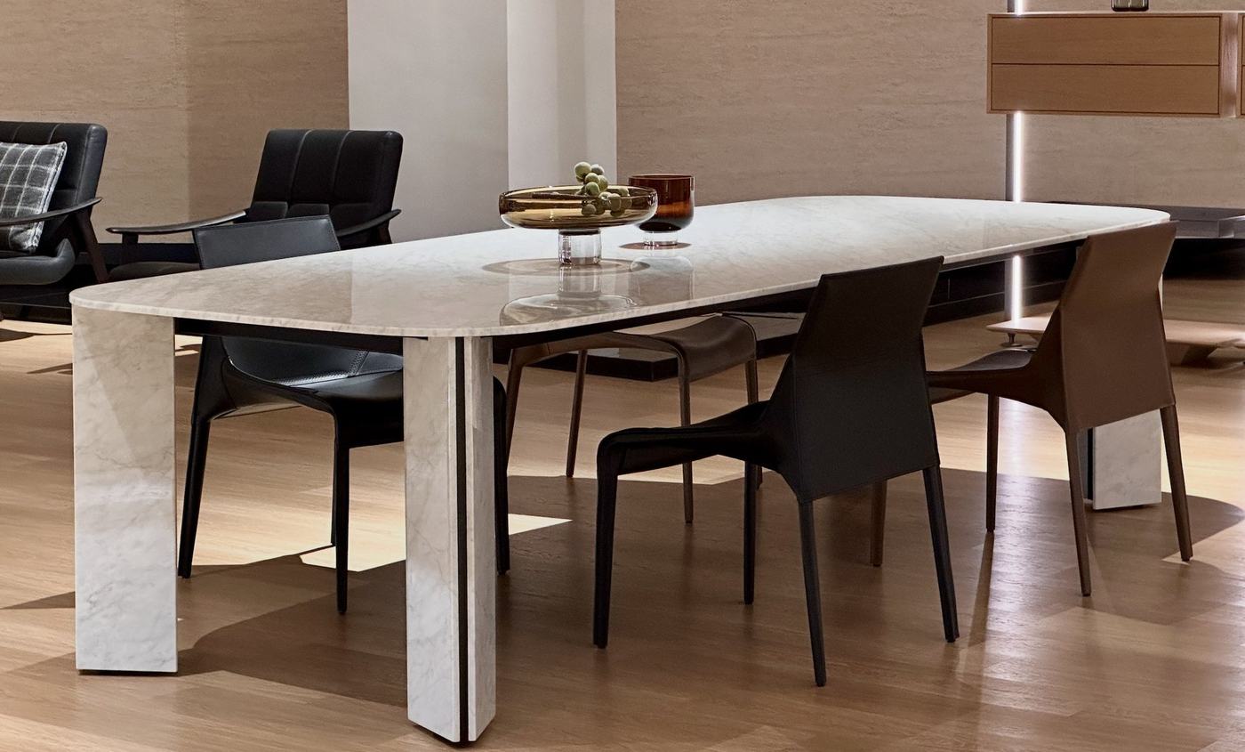 A long white marble dining table with slab legs and dark leather chairs