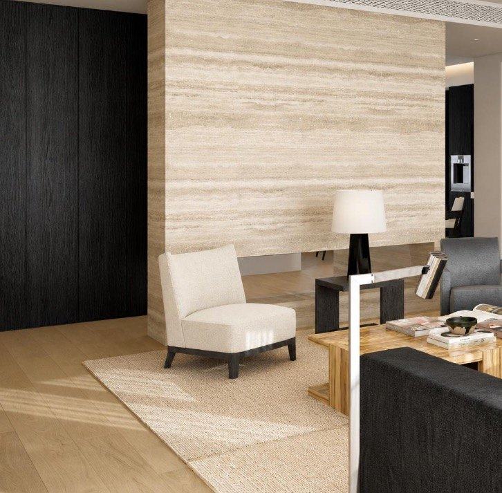 A travertine-clad wall beside floor-to-ceiling panelling in black-stained oak, with a cream lounge chair on a wool rug