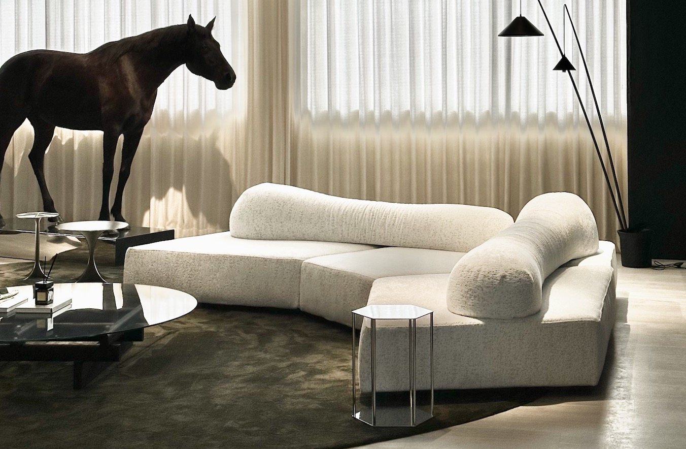 A curved ivory bouclé sofa in a room with sheer curtains and a horse sculpture