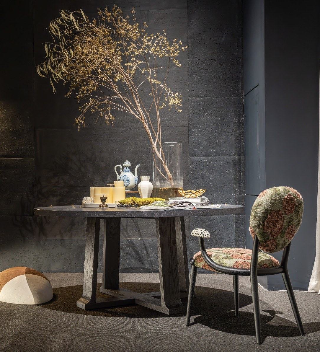A round dark oak dining table with a cross base and a floral upholstered chair