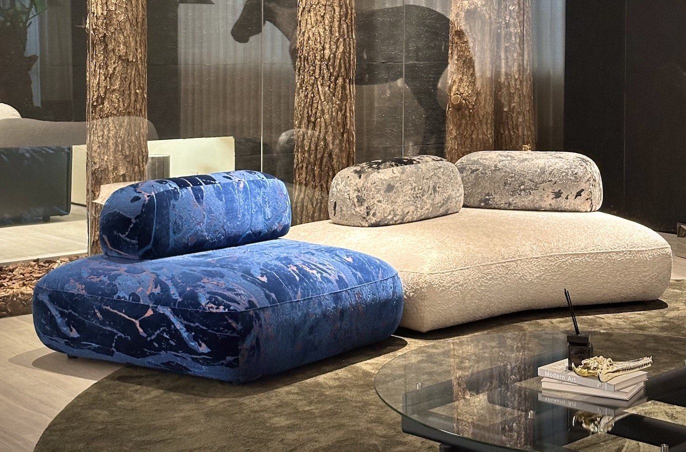 A low modular sofa in marbled deep-blue velvet beside an ivory bouclé seat